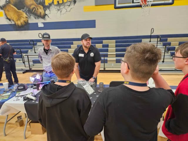 Students gathered at the LTK pest management table in a school gym