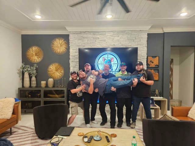 LTK members laughing as they lift one of the crew sideways in front of the LTK badge on the TV