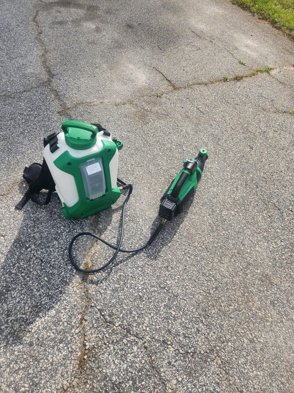 Green and white battery backpack sprayer with a handheld mister gun connected by hose on asphalt