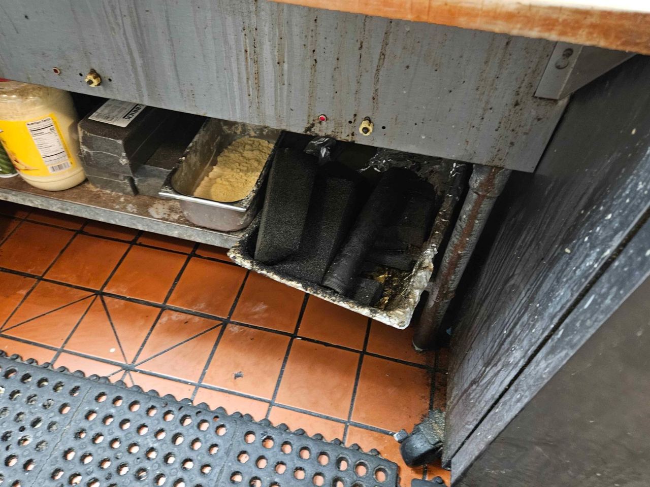 Grease and debris under a commercial kitchen prep line, the kind of finding an audit catches