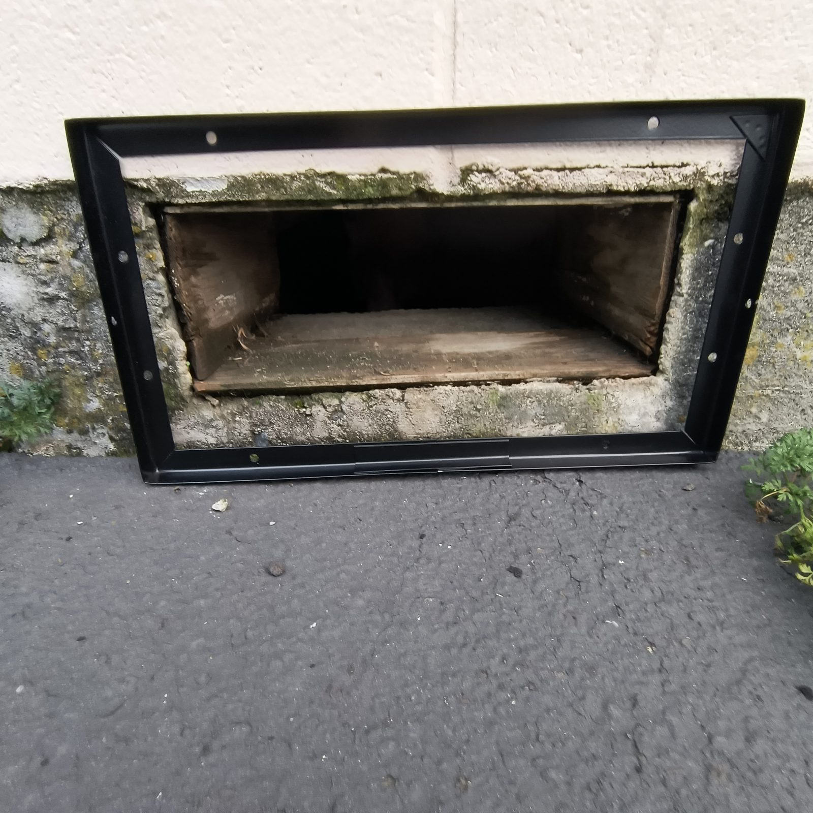 A vent cover frame being fitted around an open crawlspace vent in a block foundation